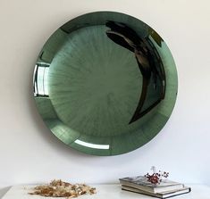 a green plate sitting on top of a white table next to a book and vase