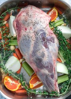 a large piece of meat in a pan with carrots, celery and onions