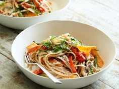 two white bowls filled with pasta and vegetables on top of a wooden table next to each other