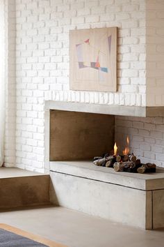 a white brick fireplace in a living room with wood logs on the floor and a painting above it