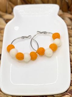 two orange and white pom - pom hoop earrings on a white plate with a basket in the background