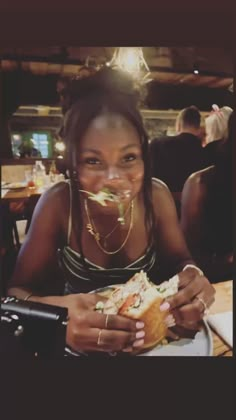 a woman sitting at a table with a sandwich in front of her face and smiling