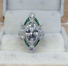 a fancy ring with green and white stones in it's center sits inside a box