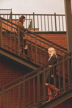 two people are walking up and down the metal stairs on top of a brick building