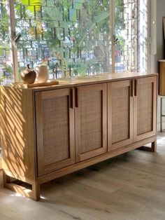 a large wooden cabinet sitting in front of a window next to a table with two vases on it