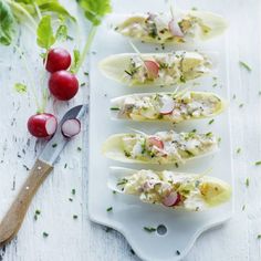 four deviled eggs with crab and radishes on a white platter next to a knife