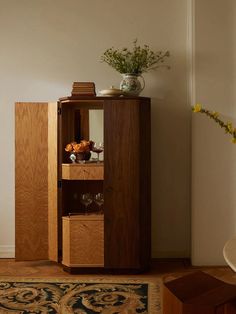 a wooden cabinet sitting on top of a hard wood floor next to a vase filled with flowers