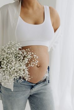 a pregnant woman holding a bouquet of baby's breath in front of her stomach