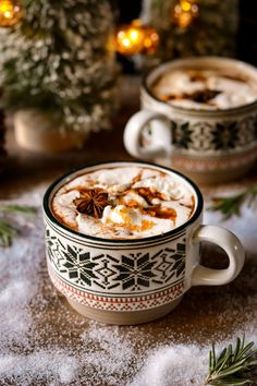 two mugs filled with hot chocolate and cinnamon on top of snow covered ground next to christmas trees