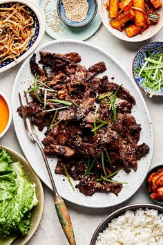 a table topped with plates of food and bowls of salad next to meat on top of rice