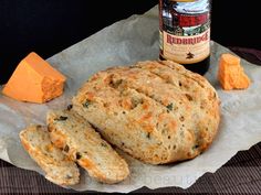 some bread and cheese are on a piece of wax paper next to a bottle of beer