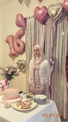 a woman standing next to a table filled with cakes and balloons