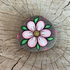 a painted rock sitting on top of a piece of wood next to a tree trunk