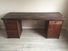 a wooden desk with two drawers on the bottom and one drawer at the top, in front of a white wall