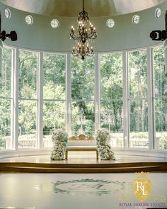 a room with large windows, chandelier and bench in front of the window