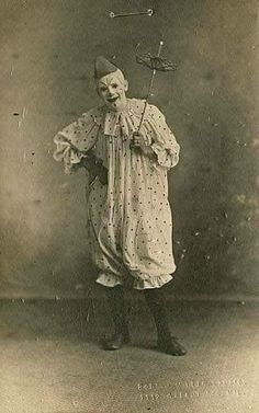 an old photo of a woman with a hat and umbrella on her head standing in front of a wall