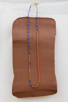 a long beaded necklace is hanging on a piece of brown fabric with blue and red beads