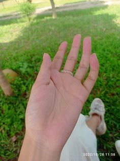 a person is holding their hand up in the air while sitting on some grass and trees