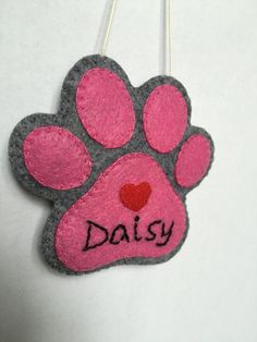 a pink and gray dog paw ornament with the word daisy written on it