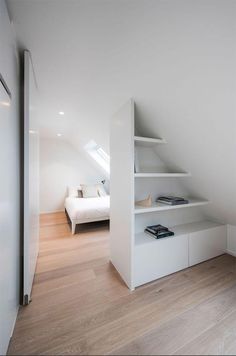 an attic bedroom with white walls and wooden flooring, built in shelving units