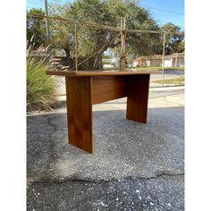 a wooden desk sitting in the middle of a parking lot next to a chain link fence