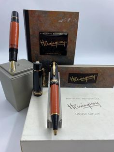 two fountain pens sitting on top of a box next to an opened book and other items