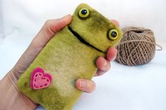 a hand holding a cell phone case with a frog on it and a ball of yarn in the background