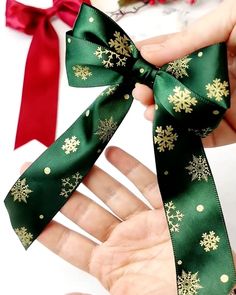 someone is holding a green ribbon with gold snowflakes on it and red bows