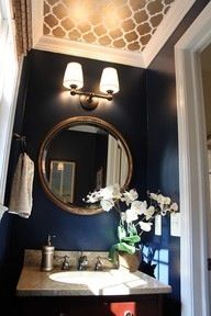 a bathroom with blue walls and white flowers on the counter top, along with a gold framed mirror