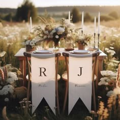 two chairs sitting in the middle of a field with flowers and candles on top of them