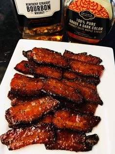 barbecue ribs on a white plate next to a bottle of bourbon