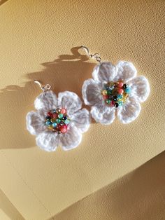 two crocheted flower earrings with beads hanging from the earwires on a yellow background