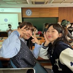 two girls posing for the camera in front of a class room