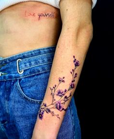 a woman's stomach with a small flower tattoo on her left arm and the word love yourself written in cursive font