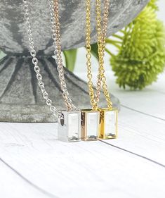 two square necklaces sitting next to each other on top of a white table with flowers in the background