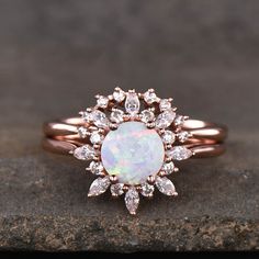 a white opal and diamond ring on top of a rock with a black background