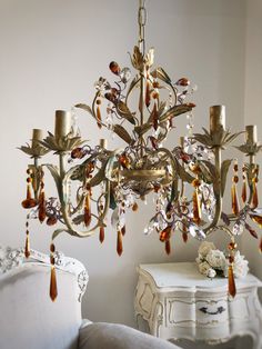 a fancy chandelier hanging from the ceiling in a room with white furniture and flowers