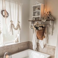 a white bath tub sitting under a window next to a shelf filled with candles and flowers