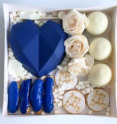 a blue heart shaped cookie in a box with white frosting and decorated cookies next to it