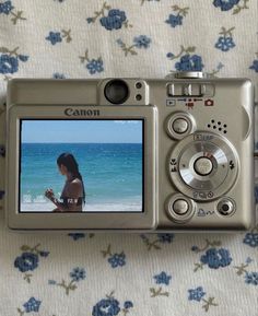 a digital camera sitting on top of a bed next to a blue flowered blanket