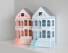 two paper houses sitting on top of a white table next to each other with windows and balconies