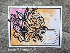 a card with flowers on it and the word hello written in white ink, sitting on top of a wooden table