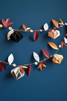 an origami garland with leaves and acorns hanging on a blue wall