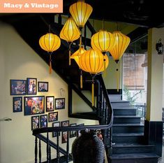 some yellow lanterns hanging from the side of a stair case with pictures on the wall