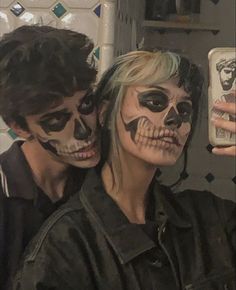 two people with face paint taking a selfie in a mirror together, one is holding a cell phone