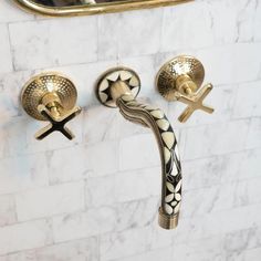 two gold faucets with crosses on them in a white tiled bathroom wall next to a mirror