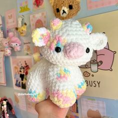 a hand holding a small stuffed animal in front of a wall with pictures on it