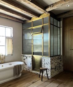 a bathroom with a bathtub and wooden flooring next to a window in the wall