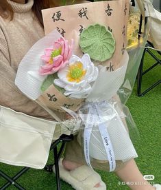 a woman sitting in a chair with flowers on her lap and holding a paper bag