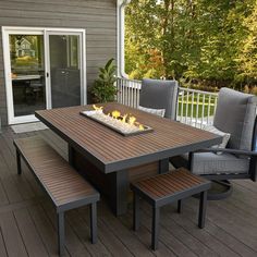 an outdoor table and chairs on a deck with fire pit in the center surrounded by trees